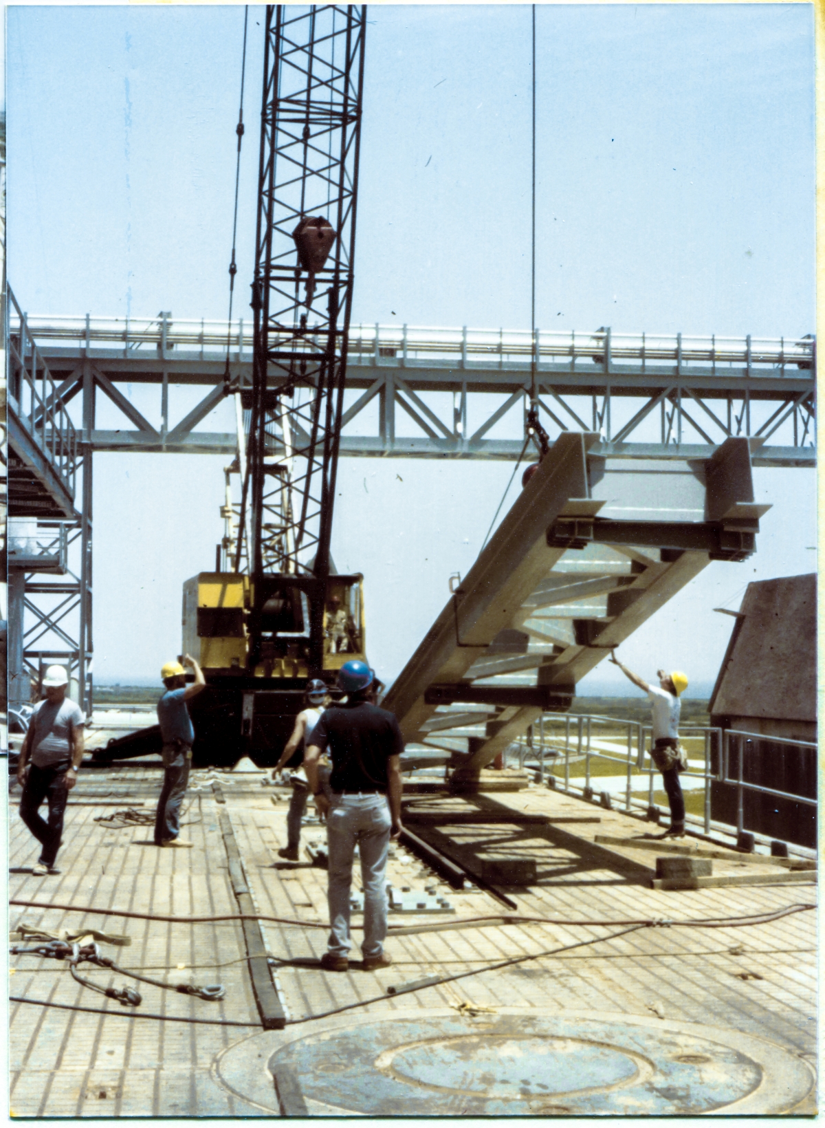 Image 071. The top of the GOX Arm Strongback has broken free of the ground and is now moving upward, signaling the sensible beginning of this lift. Wade Ivey and Rink Chiles monitor the action closely as James Dixon (partially obscured by Wade Ivey, back to camera, white tanktop) and an unknown (alas) Union Ironworker from Local 808 (far right, outstretched hand touching Strongback, yellow hardhat) also monitor the action from positions closer to the object being lifted. Photo by James MacLaren.